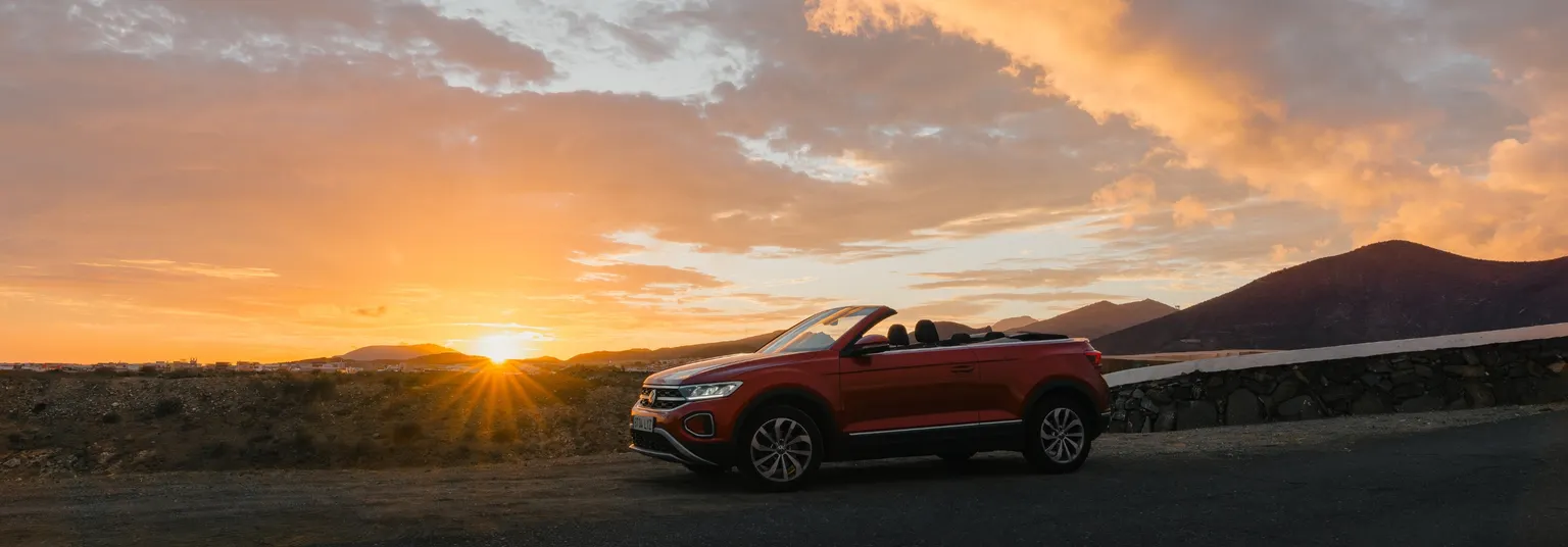 Ein Sunny Cars Mietwagen fährt an einer Küstenstraße in den Sonnenuntergang