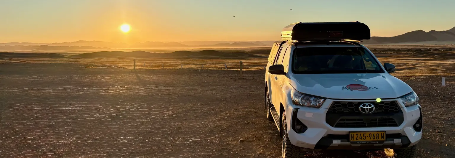 Mietwagen auf einer Schotterstraße in der Namib-Wüste bei Sonnenaufgang