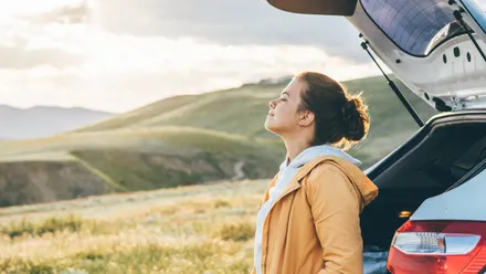 Person steht an offenem Kofferraum eines Autos in einer weiten Landschaft