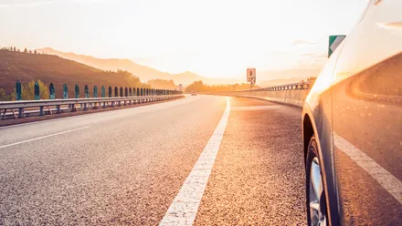 Auto fährt auf einer Straße bei Sonnenuntergang durch eine weite Landschaft