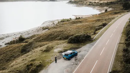 Auto steht an einer Küstenstraße neben einem See in einer bergigen Landschaft während eines Roadtrips