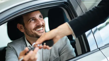 Person übergibt einen Autoschlüssel durch das Fenster eines Fahrzeugs an eine andere Person