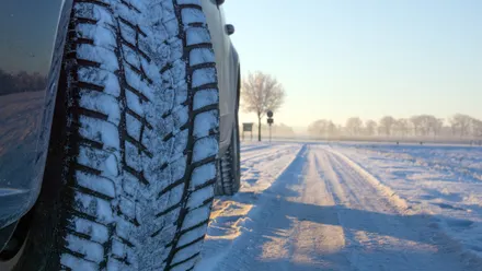 Nahaufnahme eines Autoreifens mit Winterprofil auf verschneiter Straße