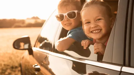 Zwei Kinder lehnen aus dem Fenster eines fahrenden Autos auf einer Landstraße während einer Reise