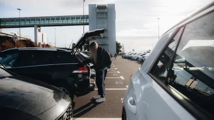 Reisende packt Gepäck in den Kofferraum eines Mietwagens auf einem Parkplatz am Flughafen