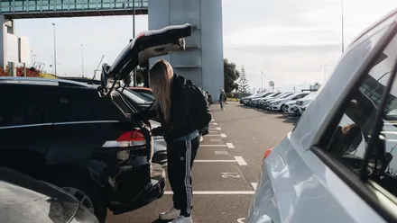 Person lädt Gepäck in den Kofferraum eines Mietwagens auf einem Parkplatz am Flughafen