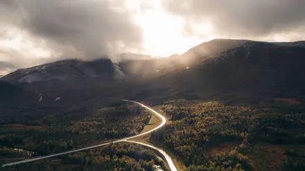 Luftaufnahme einer kurvigen Straße durch Landschaft mit Bergen und tief stehender Sonne
