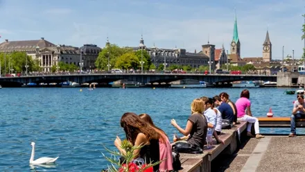 Menschen sitzen am Ufer des Zürichsees mit Blick auf die Altstadt von Zürich
