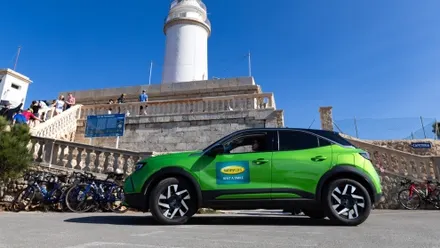 Grüner Mietwagen mit Sunny-Cars-Logo vor Leuchtturm am Cap Formentor an einem sonnigen Tag