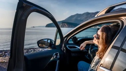 Frau parkt an einer sonnigen Küste mit geöffneter Autotür