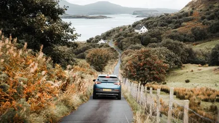 Mietwagen auf einer schmalen Landstraße mit Blick auf eine Bucht in Schottland während eines Roadtrips