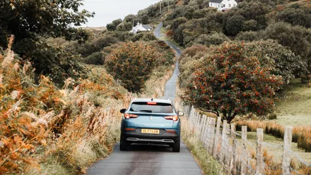 Auto fährt auf einer schmalen Straße durch eine hügelige Landschaft mit See in Schottland