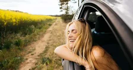 Frau schaut aus dem Fenster eines Autos, das auf einem Feld ist und lacht