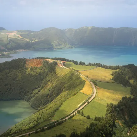 Aussicht auf die Kraterlandschaft von São Miguel mit einer kurvigen Straße, grünen Hügeln und blauem Kratersee im Hintergrund