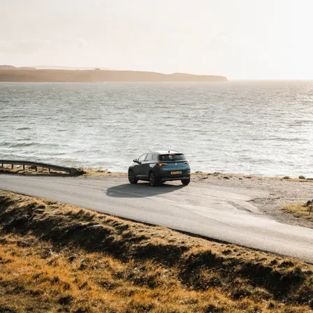 Mietwagen auf einer Küstenstraße in Schottland mit Blick auf das Meer bei tief stehender Sonne