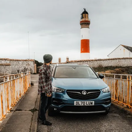 Mietwagen vor einem Leuchtturm in Schottland auf einem schmalen Weg während eines Roadtrips