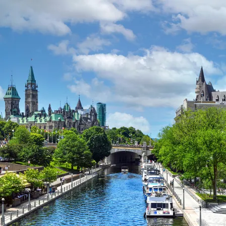 Blick auf den Rideau Canal in Ottawa mit Booten, Uferpromenade und historischen Gebäuden unter blauem Himmel