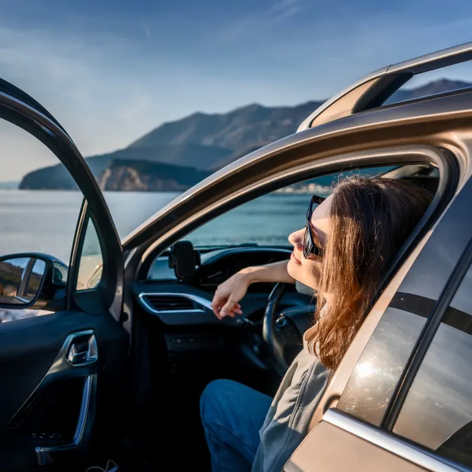 Frau parkt an einer sonnigen Küste mit geöffneter Autotür