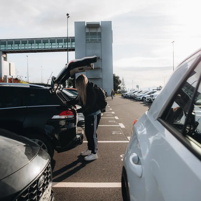 Reisende packt Gepäck in den Kofferraum eines Mietwagens auf einem Parkplatz am Flughafen