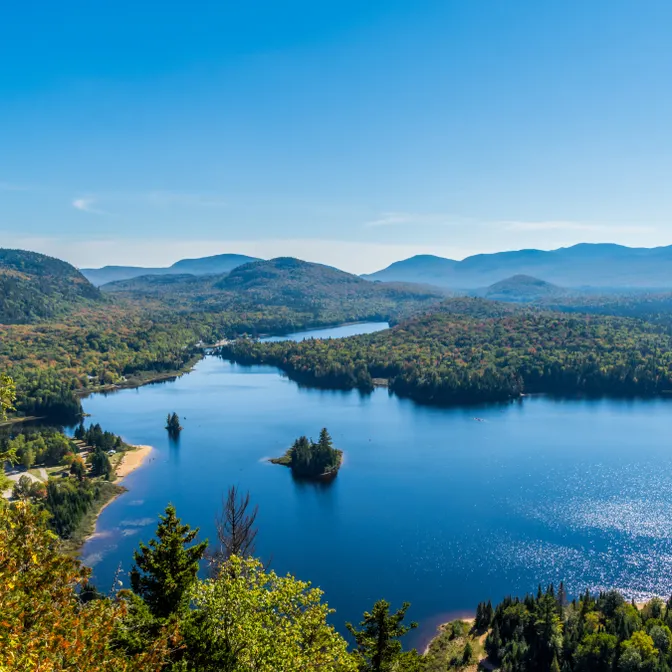 Panoramablick auf den Lac Monroe im Mont-Tremblant-Nationalpark in Québec, umgeben von bewaldeten Bergen unter blauem Himmel
