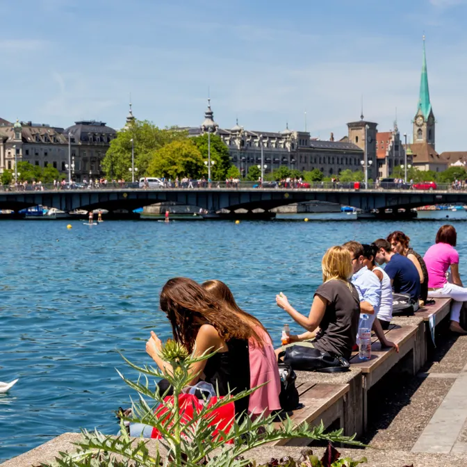 Menschen sitzen am Ufer des Zürichsees mit Blick auf die Altstadt von Zürich