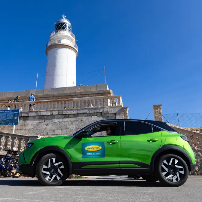 Grüner Mietwagen mit Sunny-Cars-Logo vor Leuchtturm am Cap Formentor an einem sonnigen Tag