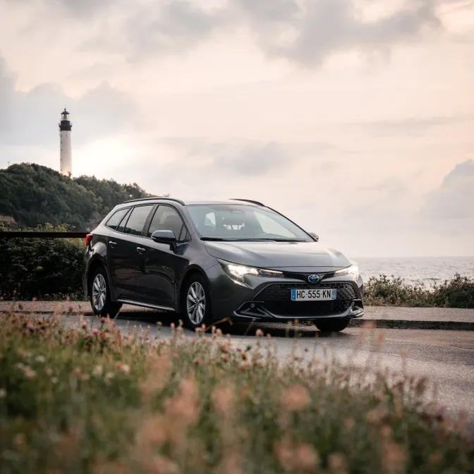 Mietwagen an der französischen Atlantikküste auf Küstenstraße mit Leuchtturm im Hintergrund