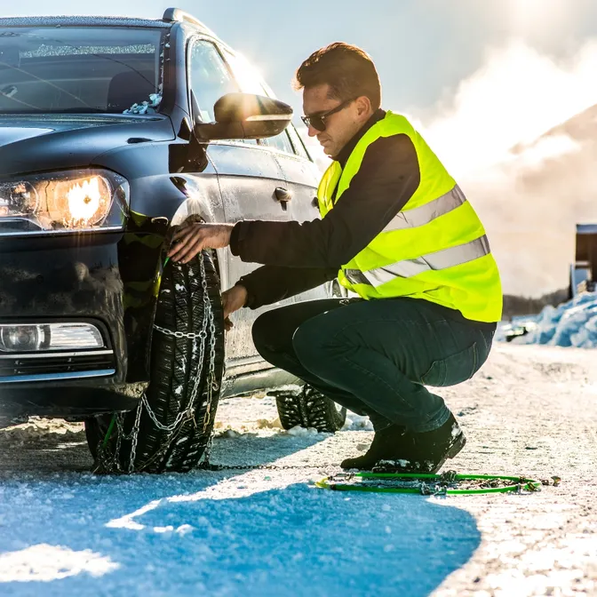 Man montiert Schneeketten an seinem Mietwagen
