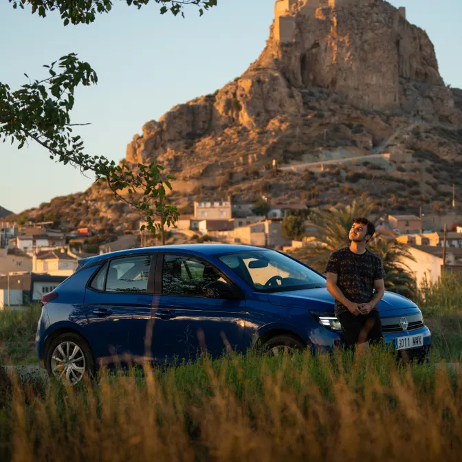 Blauer Mietwagen vor Felsenlandschaft bei Sonnenuntergang, parkend am Rand eines spanischen Dorfes