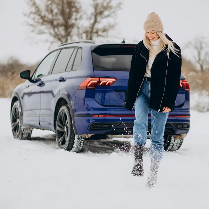 Frau steht im Winter vor Ihrem Mietwagen mit Winterreifen