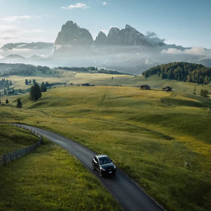 Mietwagen auf Panoramastraße durch Almwiesen im Villnößtal vor der Geislergruppe in den Dolomiten